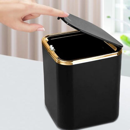 Hand pressing the button lid of a black luxury mini trash can demonstrating easy one-touch open
